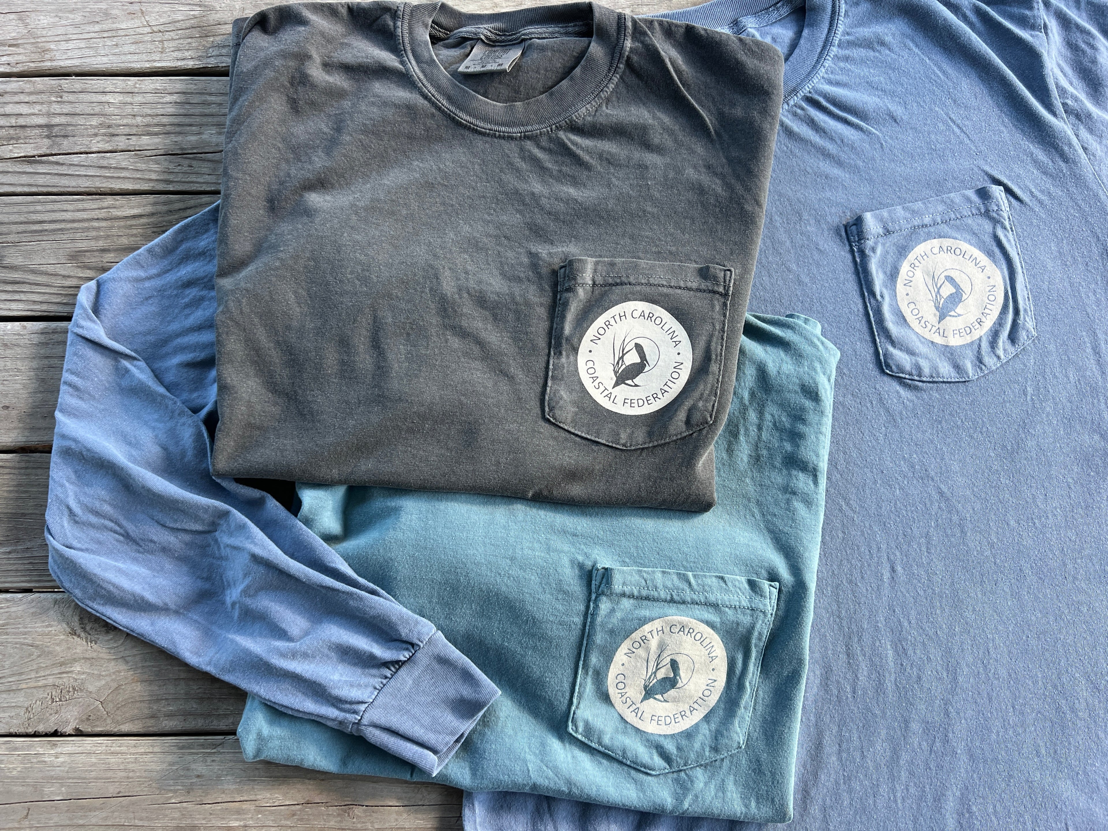 Folded blue and gray t-shirts with a logo on a wooden surface